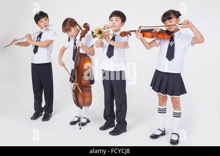 Quattro gli studenti della scuola elementare in uniformi di scuola in piedi accanto a ogni altro e la riproduzione di un classico strumento musicale ogni Foto Stock