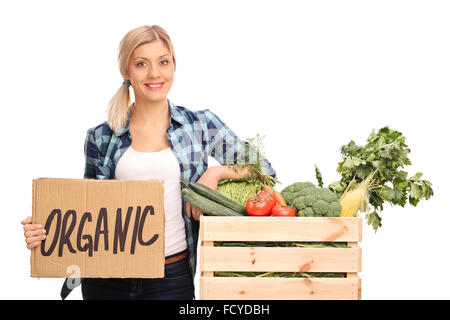 Femmina lavoratore agricolo tenendo un cartello di cartone che dice organici e appoggiato su di una cassa piena di verdure Foto Stock