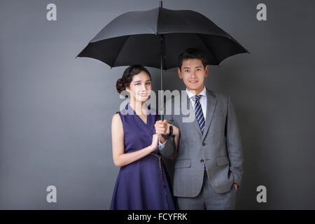 Uomo in tuta e cravatta in stile retrò e la donna in stile retrò vestito sotto lo stesso ombrello e sorridente Foto Stock