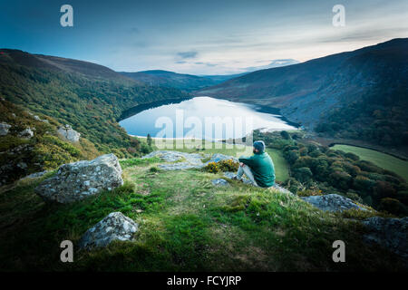 Hillwalker poggia su una collina al tramonto guardando oltre la "Guinness" lago Lough Tay e Luggala nella contea di Wicklow, Irlanda Foto Stock