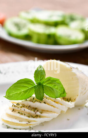 Primo piano di una lastra con fette di formaggio fresco su un tavolo e una piastra con un trito di zucchine in background Foto Stock