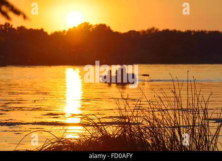 Bellissimo tramonto dorato sul fiume. Barca da pesca sullo sfondo del sole di setting Foto Stock