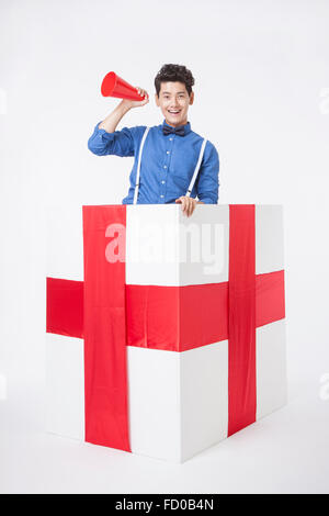 Uomo in camicia blu poste in una confezione regalo con lo sguardo in avanti e tenendo un megafono in plastica Foto Stock