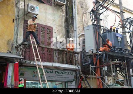 Elettricisti lavorando su cavi e una sottostazione in strada senza dispositivi di sicurezza ad Hanoi, Vietnam Foto Stock