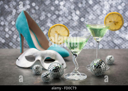 Cocktail verde con limone sul tavolo con tacco alto, maschera, e palle specchio Foto Stock