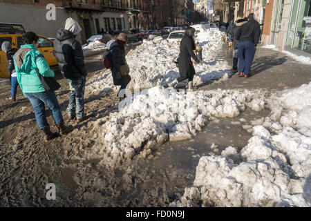 Pedoni slog attraverso pozzanghere di granite e neve mentre si recano al lavoro al mattino in corrispondenza di incroci stradali con neve dam intasato Tempesta fognature nel quartiere di Chelsea di New York lunedì, 25 gennaio 2016. Tempesta di neve Jonas oggetto di dumping 26,8 pollici su Central Park rendendo la seconda maggiore quantità poiché i record è iniziato nel 1869 e con temperature che salgono sopra il congelamento di alcuni che la neve si fonde. (© Richard B. Levine) Foto Stock