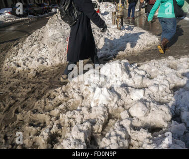 Pedoni slog attraverso pozzanghere di granite e neve mentre si recano al lavoro al mattino in corrispondenza di incroci stradali con neve dam intasato Tempesta fognature nel quartiere di Chelsea di New York lunedì, 25 gennaio 2016. Tempesta di neve Jonas oggetto di dumping 26,8 pollici su Central Park rendendo la seconda maggiore quantità poiché i record è iniziato nel 1869 e con temperature che salgono sopra il congelamento di alcuni che la neve si fonde. (© Richard B. Levine) Foto Stock