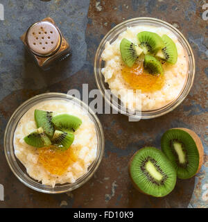 Budino di riso con pezzi di kiwi, marmellata di arancio e cannella in piccole ciotole in vetro, fotografato overhead su ardesia con luce naturale Foto Stock