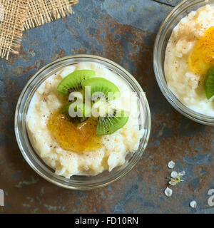 Budino di riso con pezzi di kiwi, marmellata di arancio e cannella in piccola ciotola di vetro, fotografato overhead su ardesia con luce naturale Foto Stock