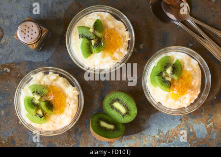 Budino di riso con pezzi di kiwi, marmellata di arancio e cannella in piccole ciotole in vetro, fotografato overhead su ardesia con luce naturale Foto Stock