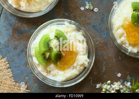 Budino di riso con pezzi di kiwi, marmellata di arancio e cannella in piccola ciotola di vetro, fotografato overhead su ardesia con luce naturale Foto Stock