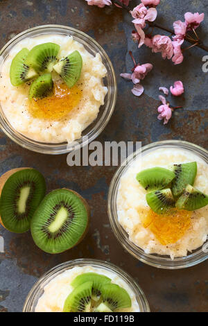 Budino di riso con pezzi di kiwi, marmellata di arancio e cannella in piccole ciotole in vetro, fotografato overhead su ardesia con luce naturale Foto Stock