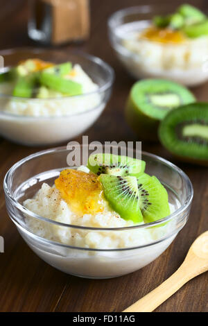Budino di riso con pezzi di kiwi, marmellata di arancio e cannella in piccole ciotole in vetro, fotografato in legno scuro con luce naturale Foto Stock