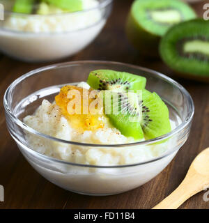 Budino di riso con pezzi di kiwi, marmellata di arancio e cannella in piccola ciotola di vetro, fotografato in legno scuro con luce naturale Foto Stock
