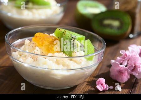 Budino di riso con pezzi di kiwi, marmellata di arancio e cannella in piccola ciotola di vetro, fotografato in legno scuro con luce naturale Foto Stock
