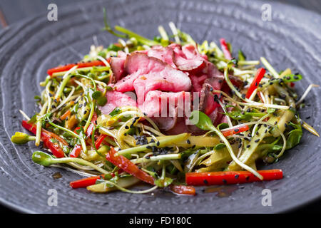 Autentica insalata con pancetta dolce peperone rosso, germogli di soia, di sesamo e di olio di oliva su una piastra nera. Mattina illuminazione atmosferica, Foto Stock