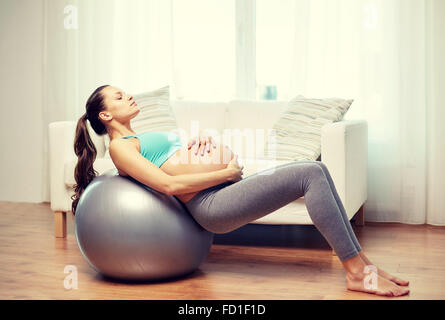 Felice donna incinta esercitando su fitball a casa Foto Stock