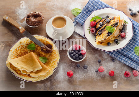 Crepes con frutti di bosco freschi, crema di cioccolato e la tazza di caffè per colazione. Vista da sopra Foto Stock