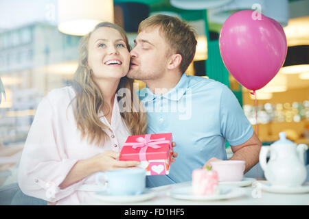 Giovane uomo baciare donna felice con giftbox in cafe Foto Stock