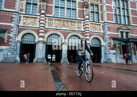 Una giovane donna trascorre una bicicletta di fronte all'ingresso al Rijksmuseum uno dei gioielli architettonici di Amsterdam Foto Stock