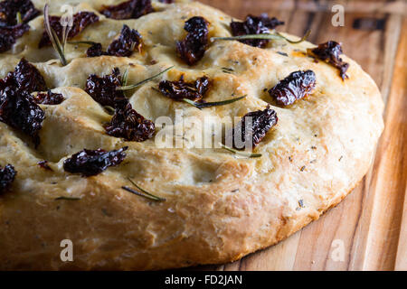 Primo piano di una casa fatta focaccia rotolo con pomodori secchi e freschi rametti di rosmarino sulla parte superiore Foto Stock