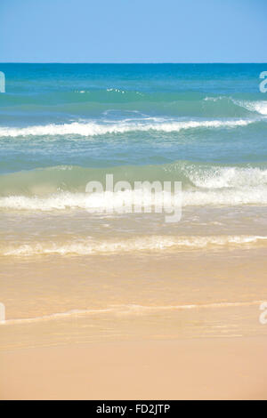 Un colorato delicatamente, vuoto vista verticale della spiaggia con un cielo blu e acqua con dolci onde che si infrangono su una spiaggia sabbiosa Foto Stock