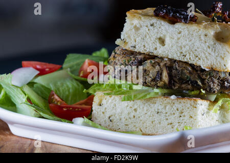 Primo piano di una casa preparato pasto vegetariano consistente in un bean burger su varie foccacia pomodoro servito con insalata Foto Stock