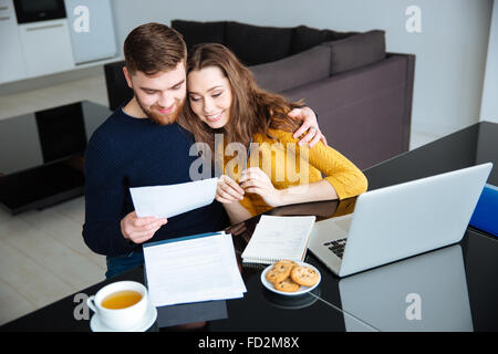 Sorridente coppia giovane gestione loro fatture a casa Foto Stock