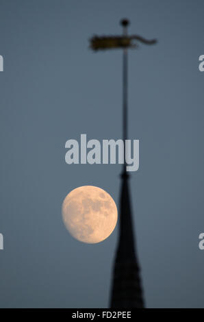 Una luna luminosa, quasi piena che sorge dietro la guglia di St. Laurence & All Saints Church, Eastwood, Southend, Essex, Regno Unito Foto Stock