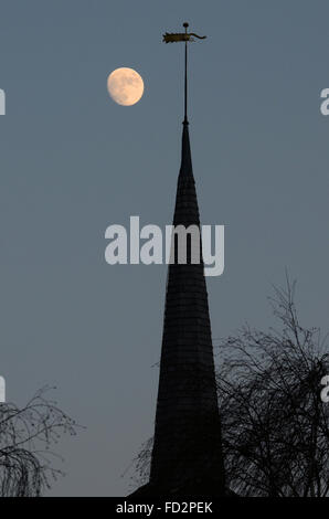 Una luna luminosa, quasi piena che sorge dietro la guglia di St. Laurence & All Saints Church, Eastwood, Southend, Essex, Regno Unito Foto Stock