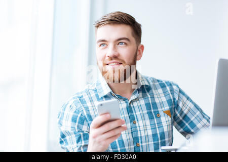 Ritratto di un uomo felice utilizza lo smartphone e guardando lontano Foto Stock