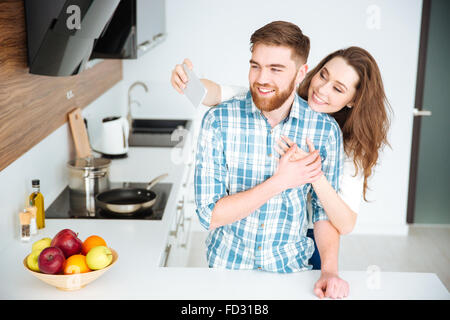 Ritratto di un giovane sorridente rendendo selfie foto sullo smartphone in cucina Foto Stock