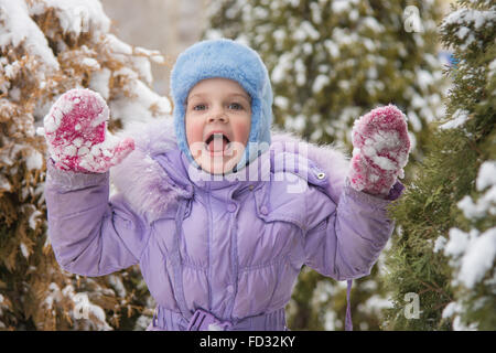 Cinque anni di ragazza in un cumulo di neve neve contro un sfondo innevato alberi Foto Stock