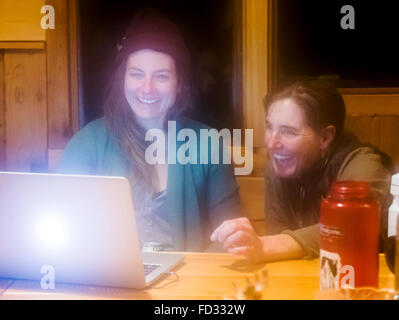 Due femmina paese indietro gli sciatori per visualizzare le fotografie sul computer laptop; all'interno di montaggio remoto Carlyle Lodge; Colombia britannica, Canada Foto Stock