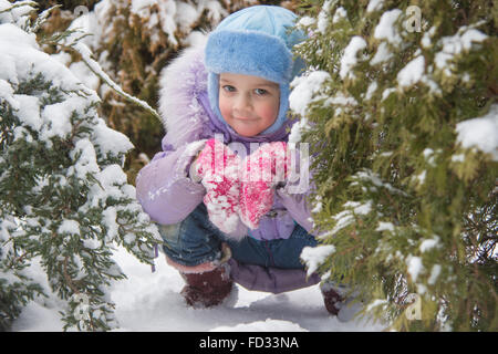 Cinque anni di ragazza in un cumulo di neve neve contro un sfondo innevato alberi Foto Stock