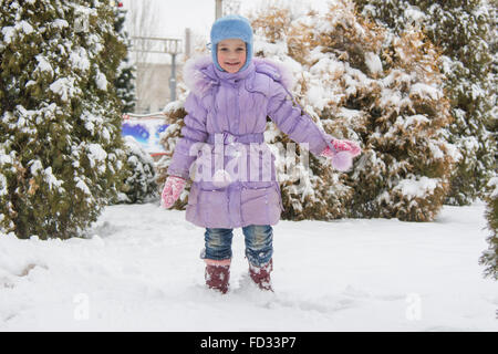 A cinque anni i costi di ragazza su un cumulo di neve neve contro un sfondo innevato alberi Foto Stock