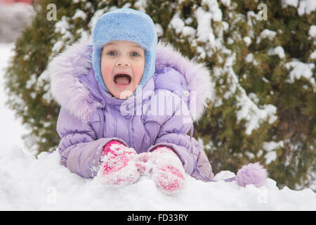 Cinque anni di ragazza giace sul cumulo di neve neve contro un sfondo innevato alberi Foto Stock