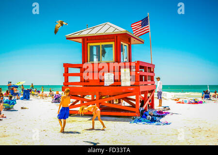 I bambini giocando sulla spiaggia in una calda giornata di sole tra le lucertole da mare vicino all'iconico rosso stazione bagnino sulla Siesta Beach, FL Foto Stock