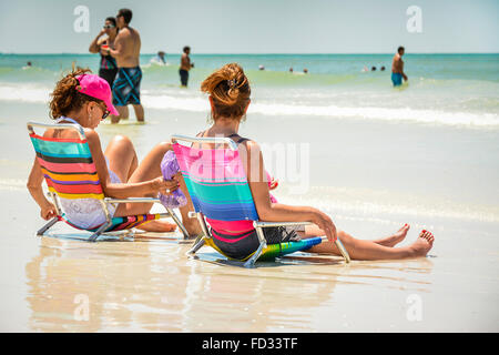 Vista lato posteriore di due donne appendere fuori a breve spiaggia sedie a navigare in bordo del relax sulla sabbia bianca sulla soleggiata giornata della Florida Foto Stock