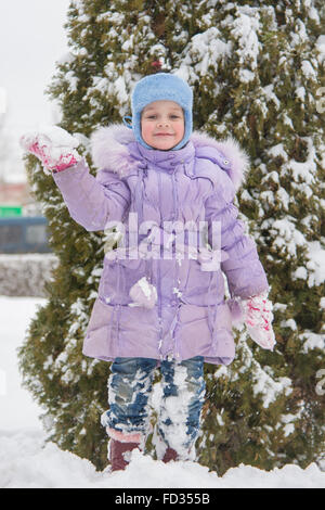 A cinque anni i costi di ragazza su un cumulo di neve neve contro un sfondo innevato alberi Foto Stock