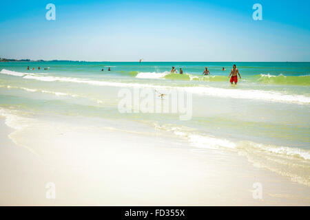 Un ampio angolo di visione di un'idilliaca spiaggia di sabbia bianca con surf e blu seascape e persone lontane scorazzare tra le onde morbide Foto Stock