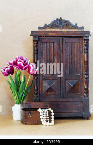 Luminose fiori viola tulipani vaso bianco, vintage vecchio armadio e cassa di legno con perle Foto Stock