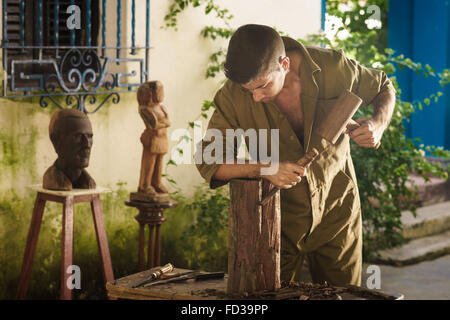 Giovane uomo al lavoro artigiano di apprendimento professione, lavorando con martello e scalpello. L'artista scolpisce un blocco grezzo di legno per fare un Foto Stock