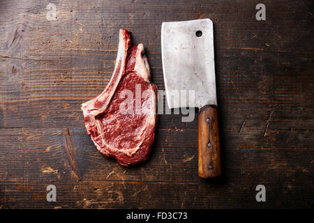 Materie carni fresche Ribeye su ossa e carne cleaver scuro su sfondo di legno Foto Stock