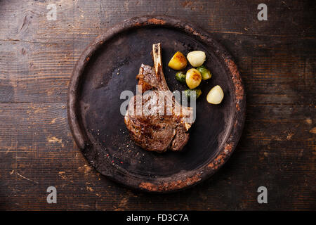 Ribeye sul tessuto osseo con verdure sulla lastra di pietra su sfondo di legno Foto Stock