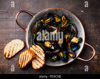 Le cozze in rame piatto di cottura e crostini di pane scuro su sfondo di legno Foto Stock