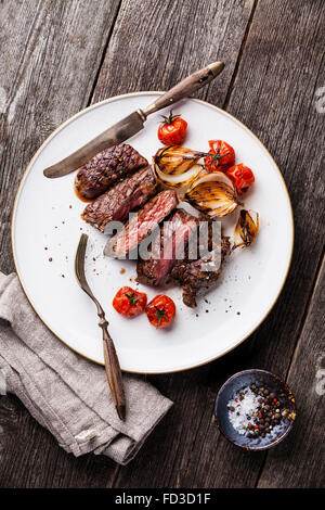 Fette di bistecca Bistecca alla griglia con cipolle e pomodori ciliegia sulla piastra su grigio Sfondo di legno Foto Stock