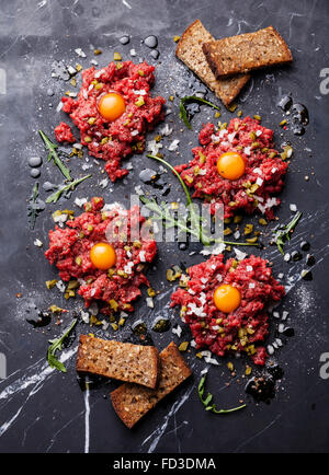 Tartare di carne di manzo con cetriolo sottaceto e cipolla fresca sul marmo scuro dello sfondo Foto Stock