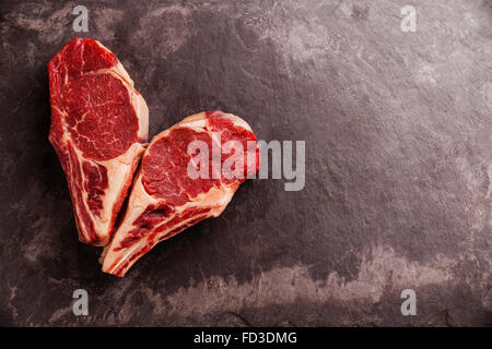 Forma di cuore crudo fresco di carne Ribeye sul tessuto osseo su pietra ardesia sfondo Foto Stock