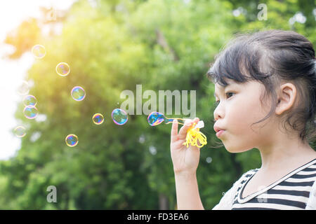 Asian bambina soffia bolle di sapone nel parco verde Foto Stock